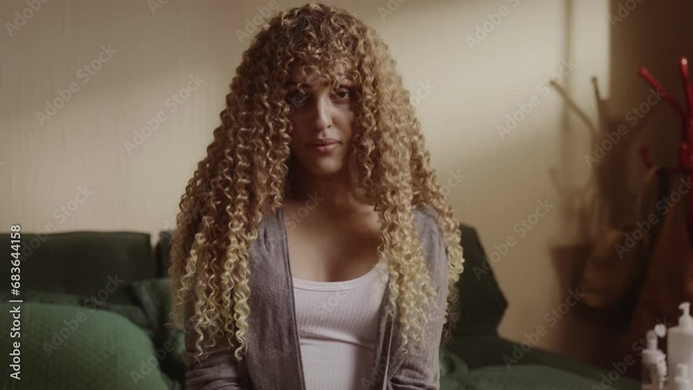 Mulher transexual jovem sentada na cama com expressao seria. Cinematico 4k.