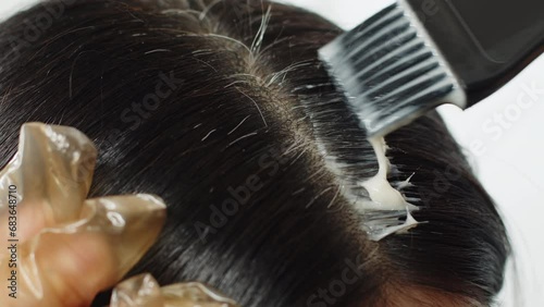 4k close up footage. Woman dyes over her gray hair, applying the product with a brush. A young brunette has silver hair. Hair care at home. Covering regrown roots. Simple treatment for dark hair.