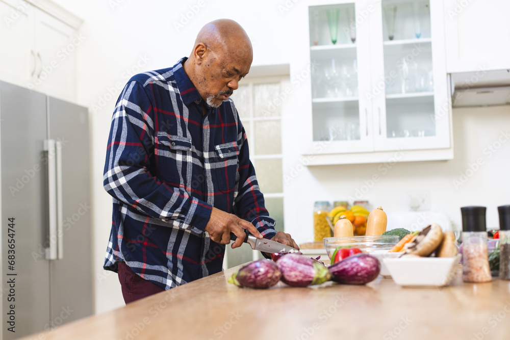 Fototapeta premium African american senior man preparing vegetables, chopping onions in kitchen