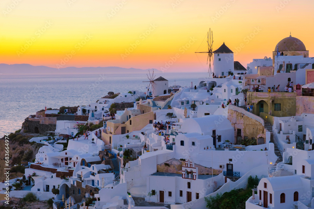 White churches an blue domes with old historical mills by the ocean of Oia Santorini Greece during sunset, a traditional Greek village in Santorini during summer