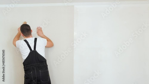 Wallpapering concept. Workman glues beige vinyl wallpaper on a non-woven backing. Renovation of the room. Hang wallpaper. Home repairs.
