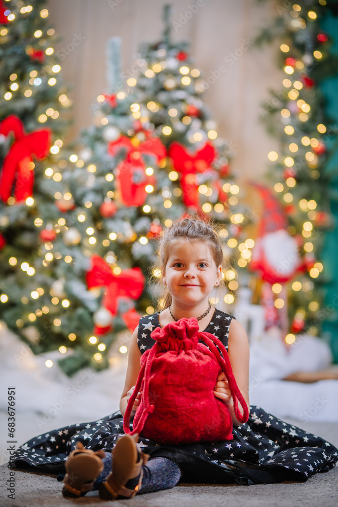 A little girl in a black dress with stars in a Christmas atmosphere. The girl is happy for Christmas. Christmas decorations.