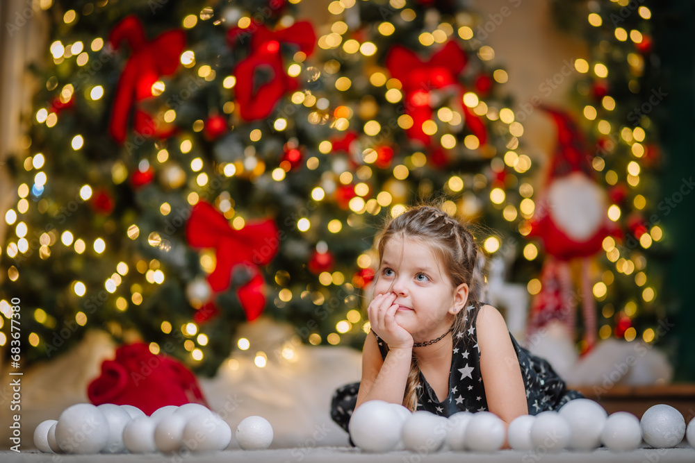 A little girl in a black dress with stars in a Christmas atmosphere. The girl is happy for Christmas. Christmas decorations. A little girl in a black dress with stars in a Christmas atmosphere. The girl is happy for Christmas. Christmas decorations.