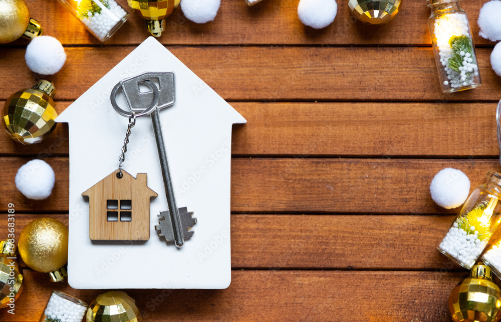 Key to house with a keychain tiny home on wooden background with Christmas decor layout. Gift for New Year, Christmas. Building, project, moving to new house, mortgage, rent and purchase real estate - obrazy, fototapety, plakaty 