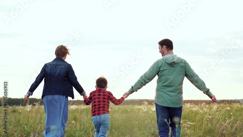 Mother and father with son run along open field with hands clasped tightly