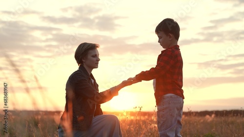 Boy extends hand to mother seeking comfort standing in grass field at sunset