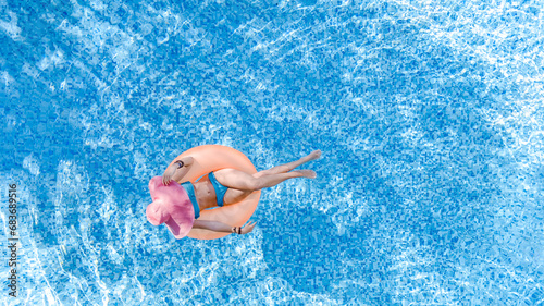 Beautiful woman in hat in swimming pool aerial drone view from above, young girl in bikini relaxes and swims on inflatable ring donut and has fun in water on tropical vacation on holiday resort 