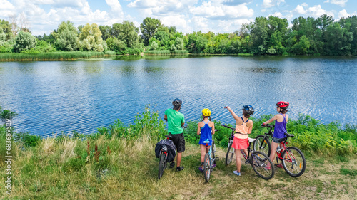 Family on bikes cycling outdoors, active parents and kids on bicycles, aerial view of family with children relaxing near beautiful river from above, sport and fitness concept
 photo