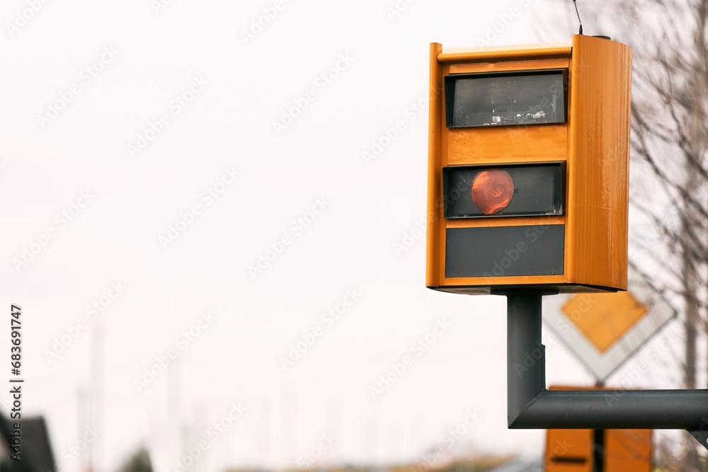A yellow speed camera flashes as it detects a speeding car on a highway