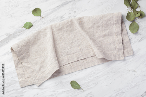 Foto Natural linen napkin folded on marble kitchen table with green leaves