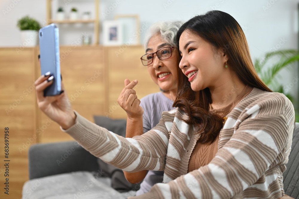 Pretty young Asian lady and mature mother taking selfie on smartphone together Pretty young Asian lady and mature mother taking selfie on smartphone together