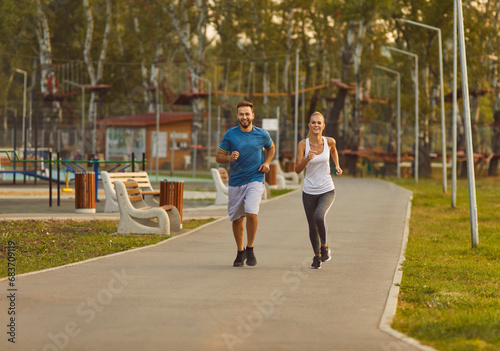 Happy smiling sporty couple wearing sportswear jogging in the park having sport workout. Young man and woman running outdoors. Workout in nature  exercising and healthy lifestyle concept.