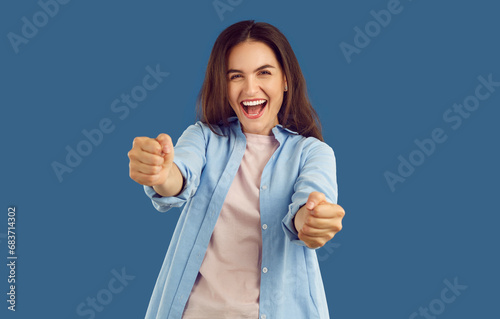 Cheerful laughing brunette young woman imagines she is driving and holding steering wheel on blue background. She is wearing blue shirt. Human emotions, energy, drive, driving transport concept.