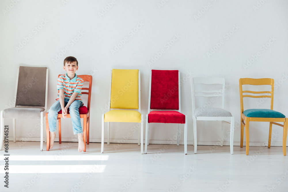 Fototapeta premium boy and many different chairs in the interior of a white room