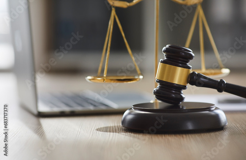 Close up gavel and sound block on wooden table, with scales of justice and laptop computer in background. Concept of legal advice and online lawyer services
