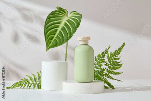 Abstract background with minimalist style for product brand presentation. A green cosmetic bottle on white cylinder podiums decorated with fern and green leaves on white background