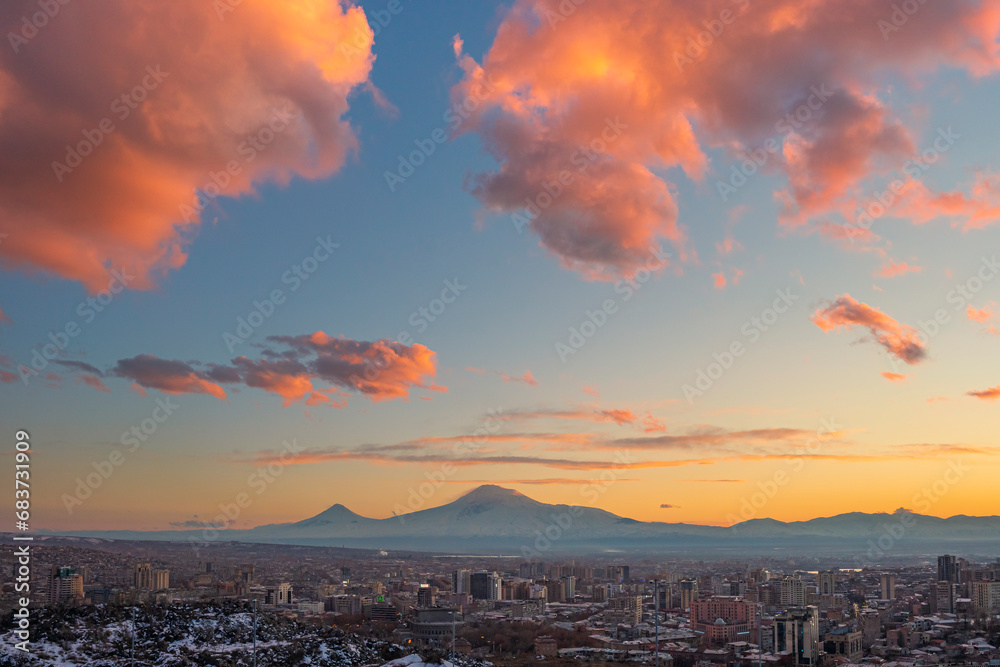 Wide angle panoramic view of the Yerevan city at sunset with the blue sky, orange clouds, and Ararat mounts