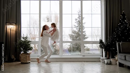 Mother and little daughter having fun together at Christmas morning. Happy family with big window at background. Christmas holidays concept. 4K, UHD photo