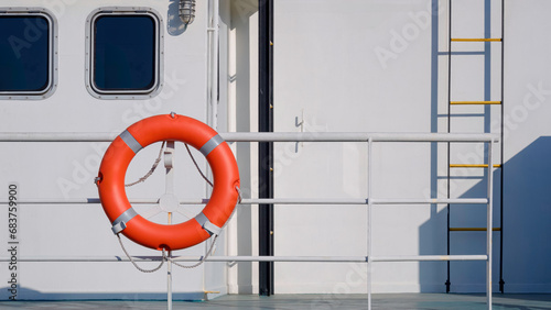 Safety orange lifebuoy hanging on steel guardrail on deck of the white ship