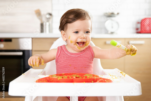 Smiling baby in high chair eating vegetable puree with spoon
