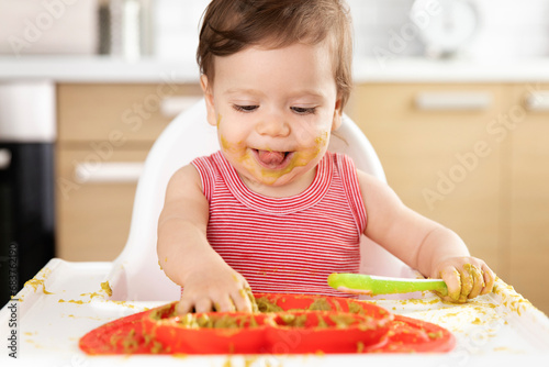Funny baby in high chair making mess with pea puree photo