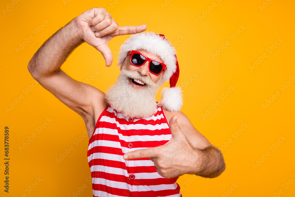 Photo of positive funny elderly guy wear new year swimsuit hat sunglass showing photo gesture empty space isolated yellow color background Photo of positive funny elderly guy wear new year swimsuit hat sunglass showing photo gesture empty space isolated yellow color background