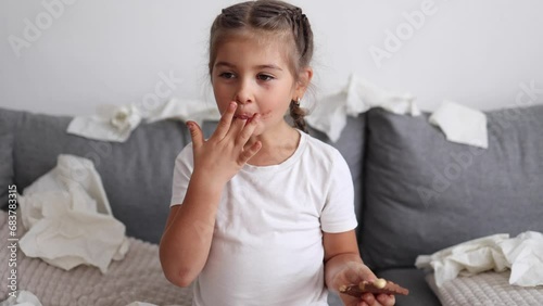Adorable and beautiful little girl eats chocolate, but it melts in her hands, so the girl licks her fingers. Sweets. Chaos on background. Mess