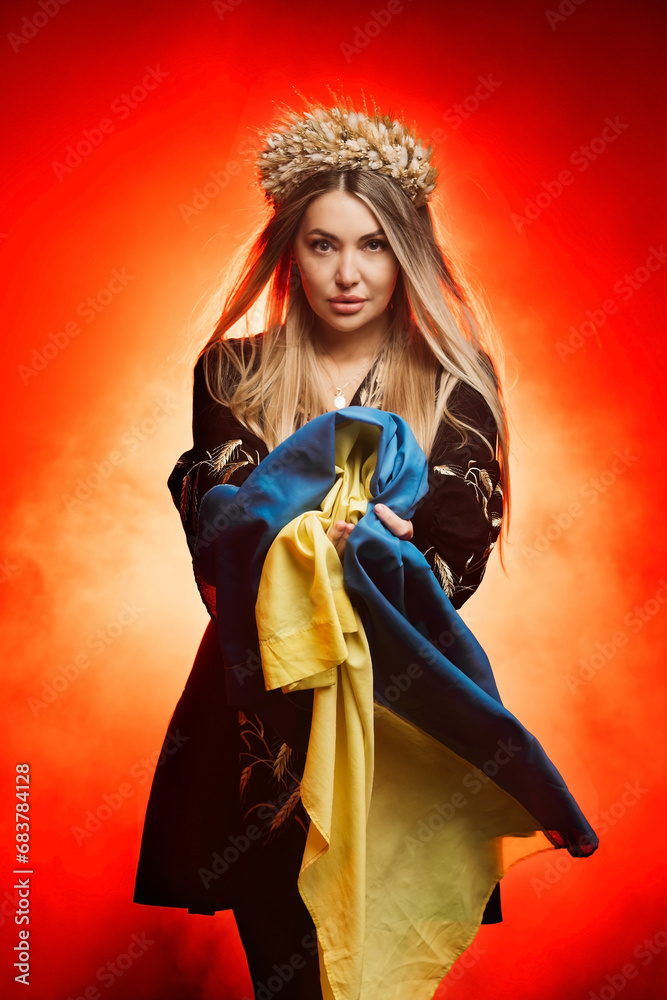 Fototapeta premium Beautiful Ukrainian woman in a national Ukrainian dress with a blue and yellow flag of Ukraine. The concept of military operations in Ukraine, national clothing and female power.