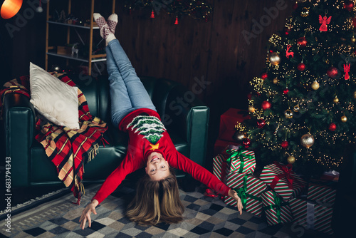 Photo of funky nice positive schoolgirl with blond hair wear red sweater lay upsaide down on couch near christmas tree at home indoors photo