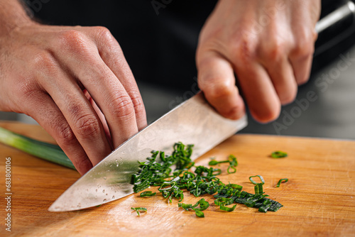 Chef chopping spring onion on wooden cutting board