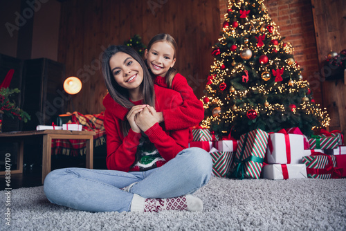Photo of positive thoughtful small sisters wear red jumpers cuddling sitting floor indoors new year north pole house © deagreez
