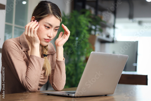 Serious tired woman beautiful Asian woman putting head in hands during using laptop computer. Thoughtful confused young female feeling stressed and having headaches while working on computer at home.