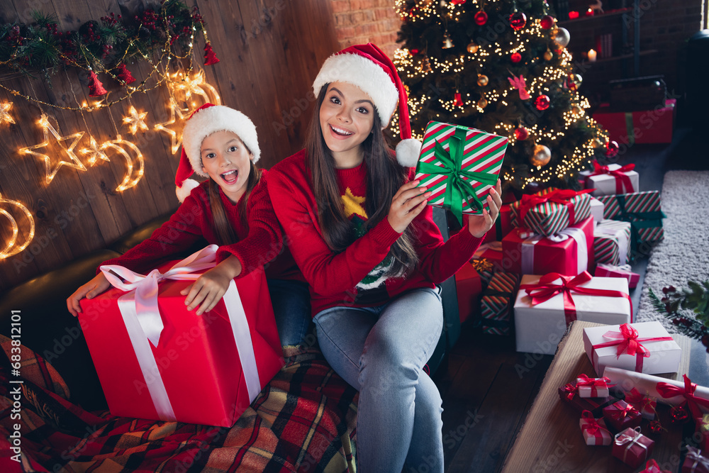 Photo of shiny impressed small sisters wear red ugly print new year pullover packing gifts indoors apartment room