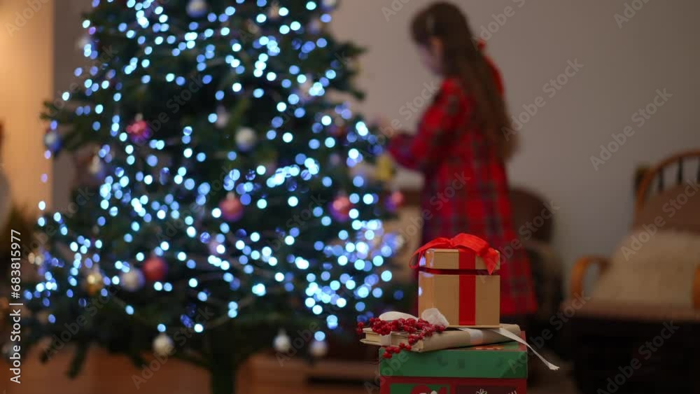 Christmas gifts. In the background, out of focus, a girl decorates a Christmas tree Christmas gifts. In the background, out of focus, a girl decorates a Christmas tree