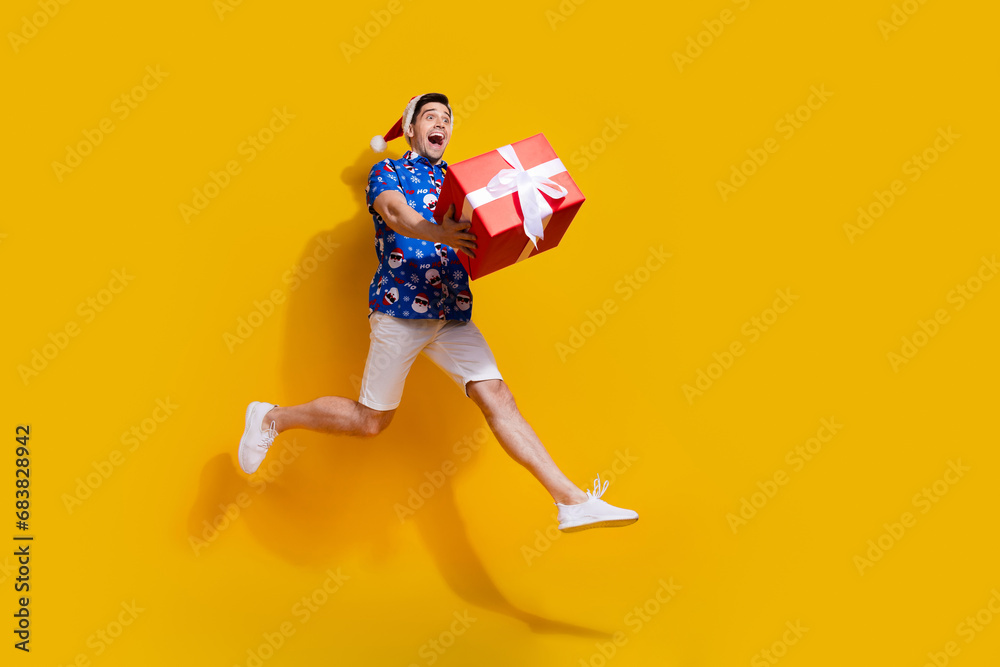 Obraz premium Full size photo of impressed energetic guy jump arms hold newyear giftbox empty space isolated on yellow color background