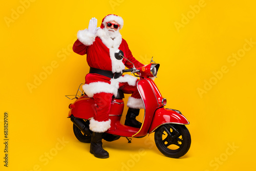 Full body profile photo of charismatic aged santa drive bike arm palm waving hi new year greetings isolated on yellow color background