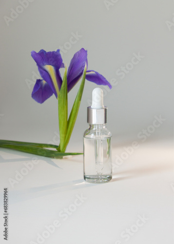 glass bottle with a pipette for cosmetics on a background of iris flowers