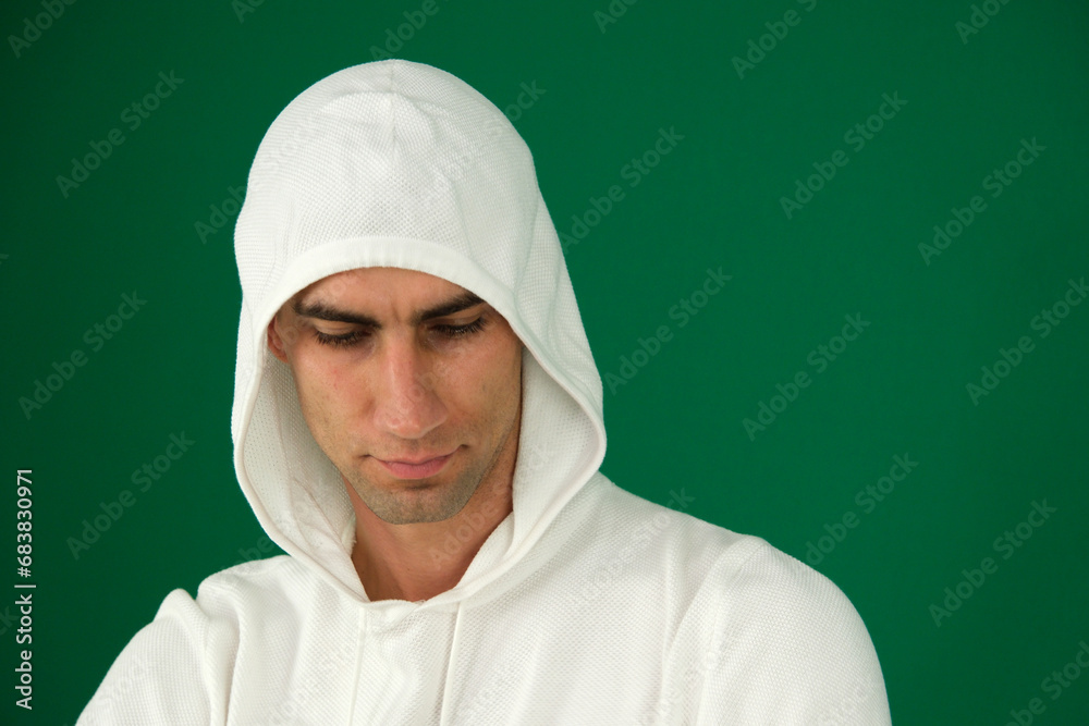 emotions of a handsome man guy on a green background chromakey close-up dark hair young man. white sweatshirt the process of putting on a hooded sweatshirt by a young man in white clothes emotions of a handsome man guy on a green background chromakey close-up dark hair young man. white sweatshirt the process of putting on a hooded sweatshirt by a young man in white clothes
