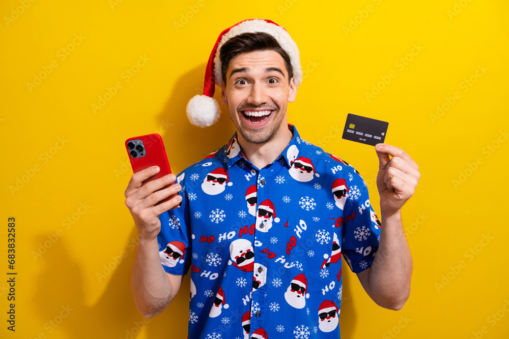 Photo of guy cashless service hold smartphone plastic credit card excited santa claus hat online shop isolated on yellow color background Photo of guy cashless service hold smartphone plastic credit card excited santa claus hat online shop isolated on yellow color background