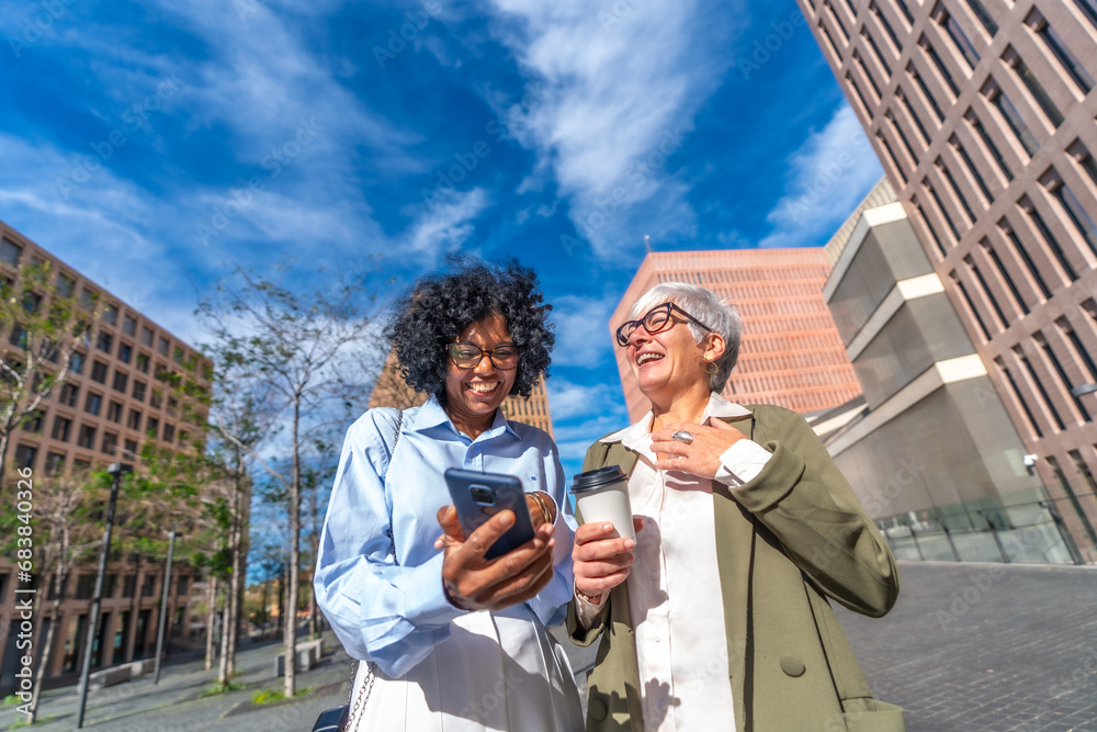 Fototapeta premium Multi-ethnic businesswomen laughing while using phone outdoors