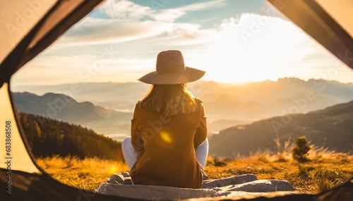 Camping in the wilderniss: Young woman with hat sitting in front of her tent on the moutain and enjoys the sunset in golden light. travel and adventure concept