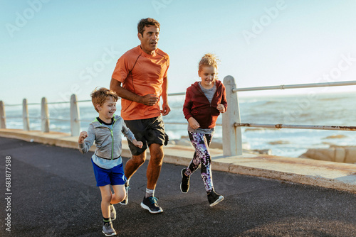 Father jogging with his kids by the ocean photo