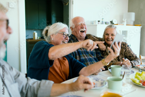 Senior Friends Laughing and Looking at Smartphone During Lunch