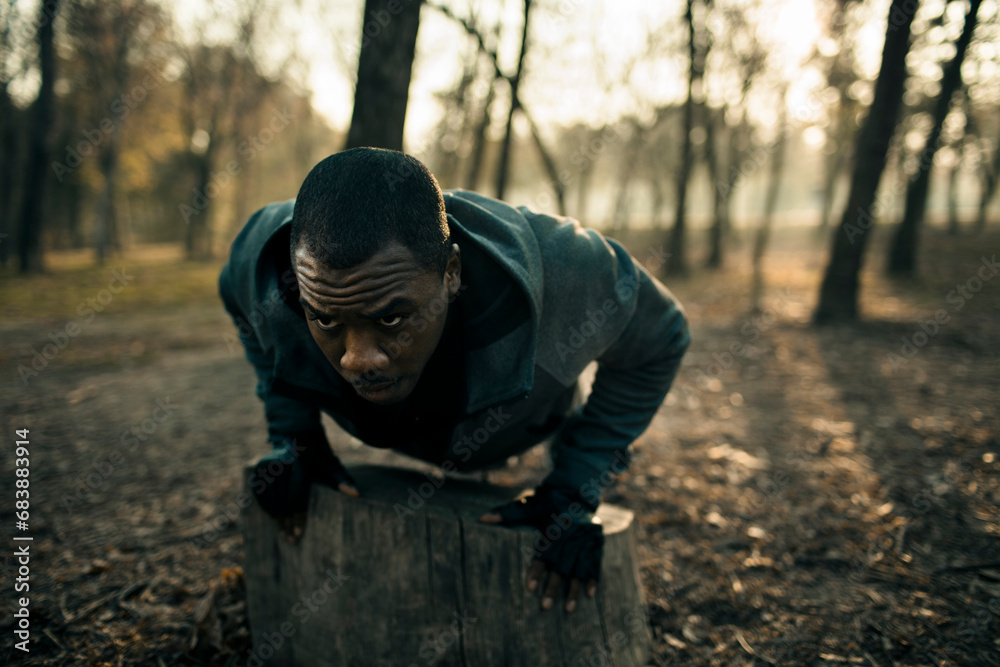 Athletic young man doing push ups on tree stump in nature park Athletic young man doing push ups on tree stump in nature park