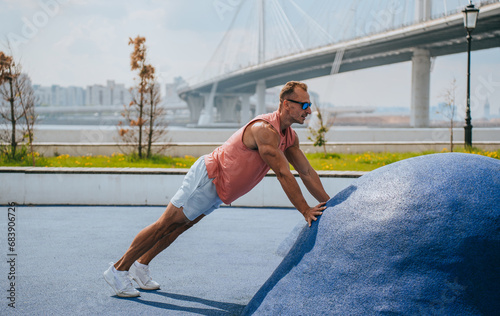A professional athlete trains outdoors, does push-ups to get dressed, sportswear, sunglasses on the background of the big bridge of the city. Sports fitness healthy lifestyle