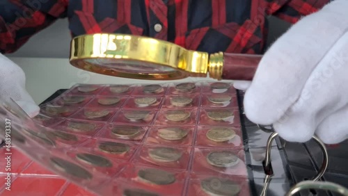 Numismatist in gloves examines collection of coins through magnifying glass. Collecting and valuing coins photo