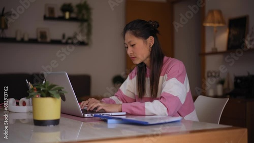 Side view of a student Chinese woman studying from home using a laptop to do her homework. Copy space. photo