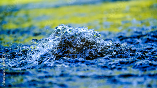 Water droplets / watercourse with reflections in the sunlight. Wonderful play of colours in small drops of water in a stream in the sun. Close-up taken in sunshine on the bank.