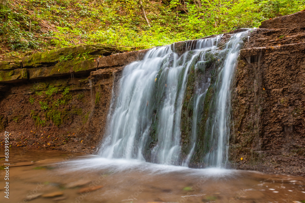 Obraz premium Scenic waterfall in a mountain stream in the forest. One of the waterfalls of the cascade of Rusiliv waterfalls. Rusyliv, Ternopil Region, Ukraine