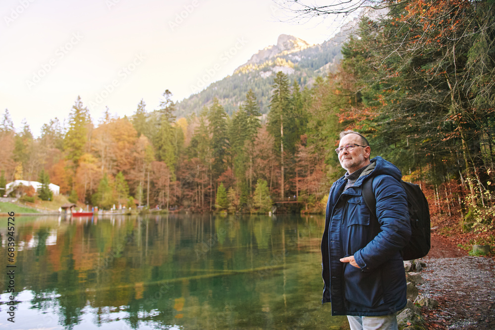 Fototapeta premium Outdoor portrait of handsome mature man enjoying nice day outside, visiting small mountain lake, fall season